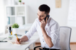 man on phone while writing in notebook