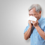 older man sneezing into tissue