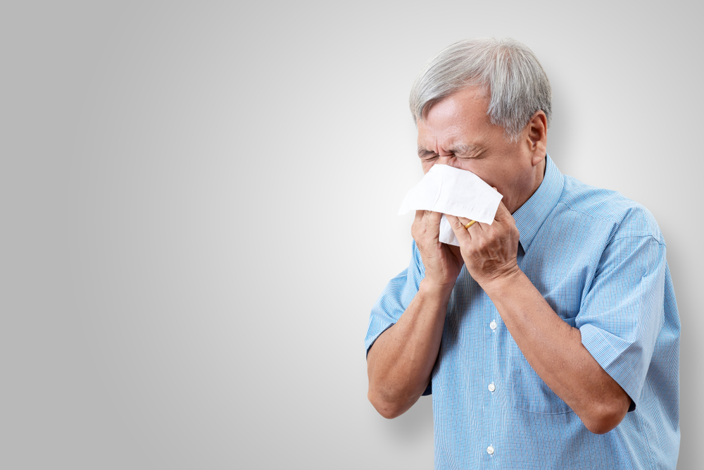 older man sneezing into tissue