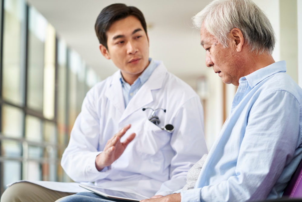 young asian doctor talking and explaining test result and diagnosis to demoralized elderly patient in hospital hallway