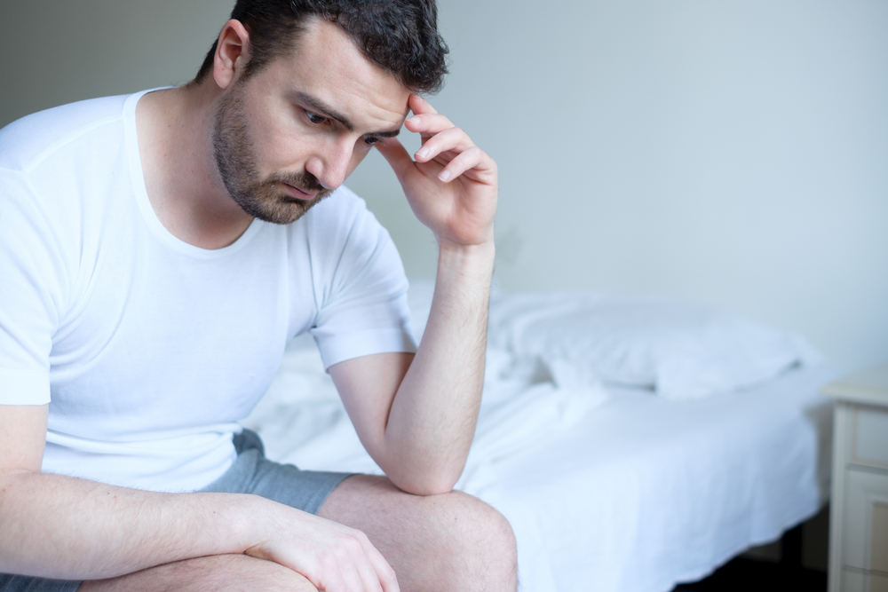 man sitting at the end of the bed upset